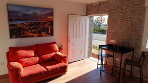 Una habitación con un sofá rojo, una mesa de comedor con sillas, una pared de piedra y una puerta que da al exterior.