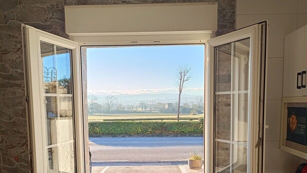 Una habitación con pared de piedra, lavadora, silla y ventana que ofrece vistas abiertas a una carretera y campos.