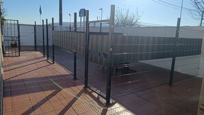 Un espacio exterior cercado con suelo de baldosas, una reja metálica y una farola.
