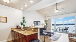 Amplia sala de estar con cocina, mesa de comedor y un balcón con vista al agua.