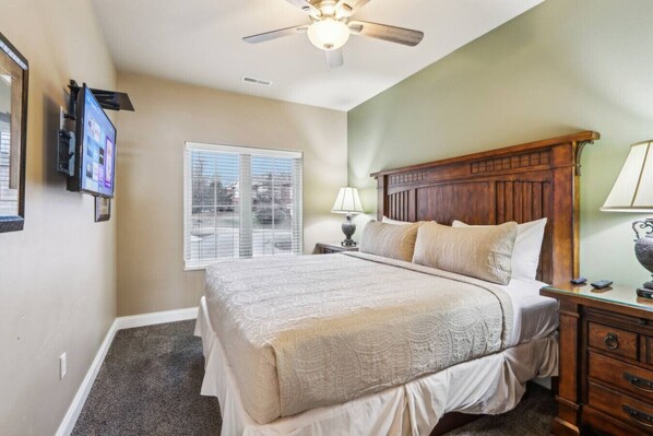 A bedroom with a bed, a nightstand, a lamp, a ceiling fan, and a window with blinds.