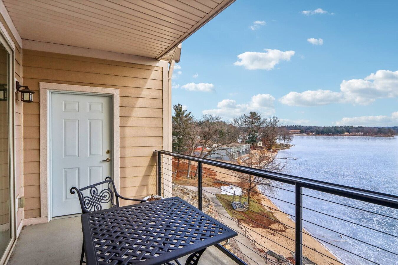 En balkon med et bord og stole, der ud til et frossent vandområde med en fjerntliggende kystlinje.