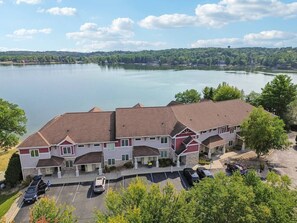 A two-story hotel with a red and white facade, parking lot, and a view of a lake.