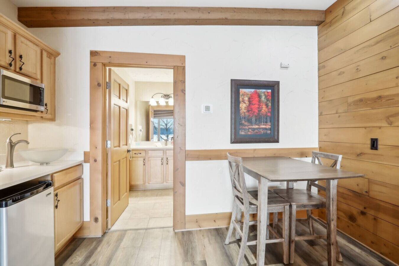 A kitchen with wooden cabinets, a microwave, and a sink. There is a dining table with chairs.