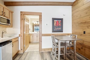 A kitchen with wooden cabinets, a microwave, and a sink. There is a dining table with chairs.