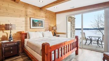 A wooden bedroom with a large bed, wooden nightstands, a table by the window, and a view of a lake.