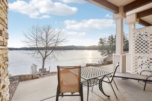 A patio with a table and chairs overlooking a lake, with a stone wall and a lattice fence in the background.