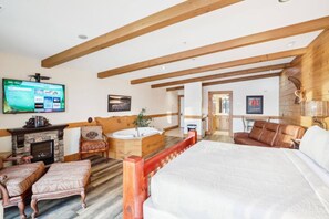 A spacious bedroom with a large bed, a wooden ceiling, a fireplace, a TV, and a bathroom with a bathtub.