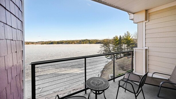 En balkon med udsigt over en frossen sø, metalstole og et lille rundt bord.