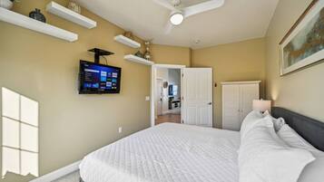 Une chambre à coucher avec un lit, un ventilateur de plafond, un téléviseur fixé au mur et une porte donnant sur une autre pièce.