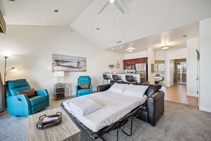 Une chambre d’hôtel moderne équipée d’un lit, de deux fauteuils, d’un bureau et d’une kitchenette.