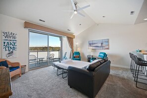 Une pièce spacieuse comprenant un grand lit, un canapé et un coin repas. Un balcon offre une vue sur le lac.