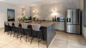 A modern kitchen with a central island, bar stools, stainless steel appliances, and a herringbone-patterned backsplash.