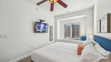 A bedroom with a bed, a ceiling fan, a TV mounted on the wall, and a window with blinds.