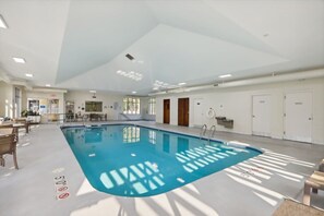 Une piscine intérieure avec des marquages bien visibles, un plafond laissant passer la lumière du soleil et un espace détente avec des tables et des chaises.