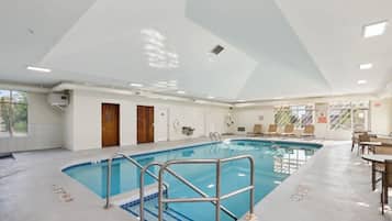 An indoor swimming pool with clear lanes, a lifeguard chair, and a poolside area with tables and chairs.