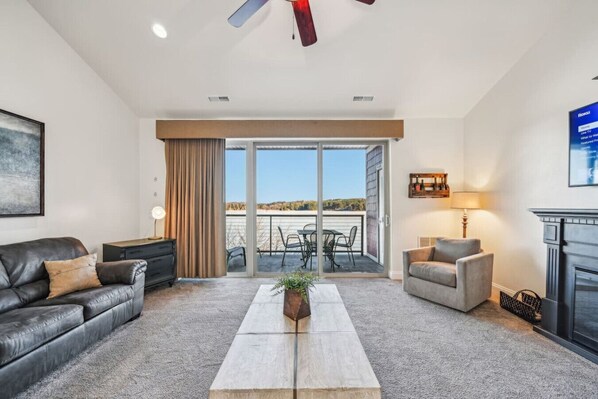 Un salon moderne avec un canapé en cuir, une table basse en bois et une cheminée. Une porte-fenêtre coulissante donne accès à un balcon aménagé avec du mobilier d’extérieur.