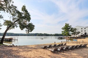A lakeside view with a sandy beach, lounge chairs, a dock, and a building in the background. - Beachview Twin #2 at Delton Grand (429) (Wisconsin Dells)