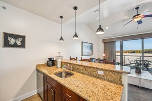 A modern kitchen with granite countertops, stainless steel sink, pendant lighting, and a view of the outdoors through large windows. - Beachview Twin #2 at Delton Grand (429) (Wisconsin Dells)
