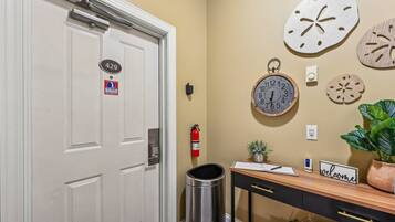 A hotel room entrance with a white door marked "429", a wall clock, a small desk with a welcome sign, a fire extinguisher, and a trash bin.