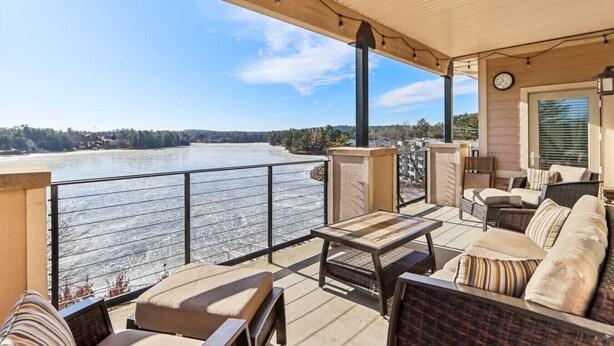 Een overdekt terras buiten met zitplaatsen, een klok en uitzicht op een rivier.