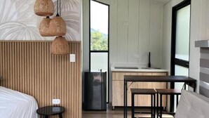 A modern hotel room with a bed, a sofa, a small table, a kitchen area, and a large window. - Cocora Valley Cabin (Quindío)