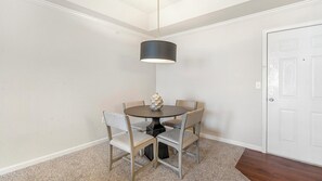A dining area with a round table, four chairs, a vase, and a pendant light.