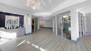A spacious lobby with a reception desk, modern pendant lighting, and glass doors leading to other areas.
