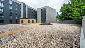 A courtyard with a gravel path, modern buildings, and a bench. - Modern 2bed Manchester+ parking (Manchester)