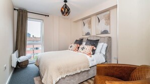 A bedroom with a bed, a brown leather chair, a window with curtains, and artwork on the wall. - Modern 2bed Manchester+ parking (Manchester)