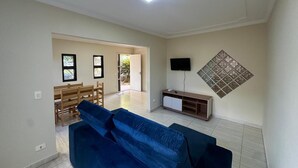 A living room with a blue sofa, a TV on the wall, and a wooden cabinet. - Complete House Near the Airport (Jardim Petropolis Campo Grande)