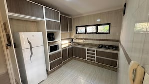 A modern kitchen with a built-in refrigerator, stove, and sink, featuring wooden cabinets and a tiled backsplash. - Complete House Near the Airport (Jardim Petropolis Campo Grande)