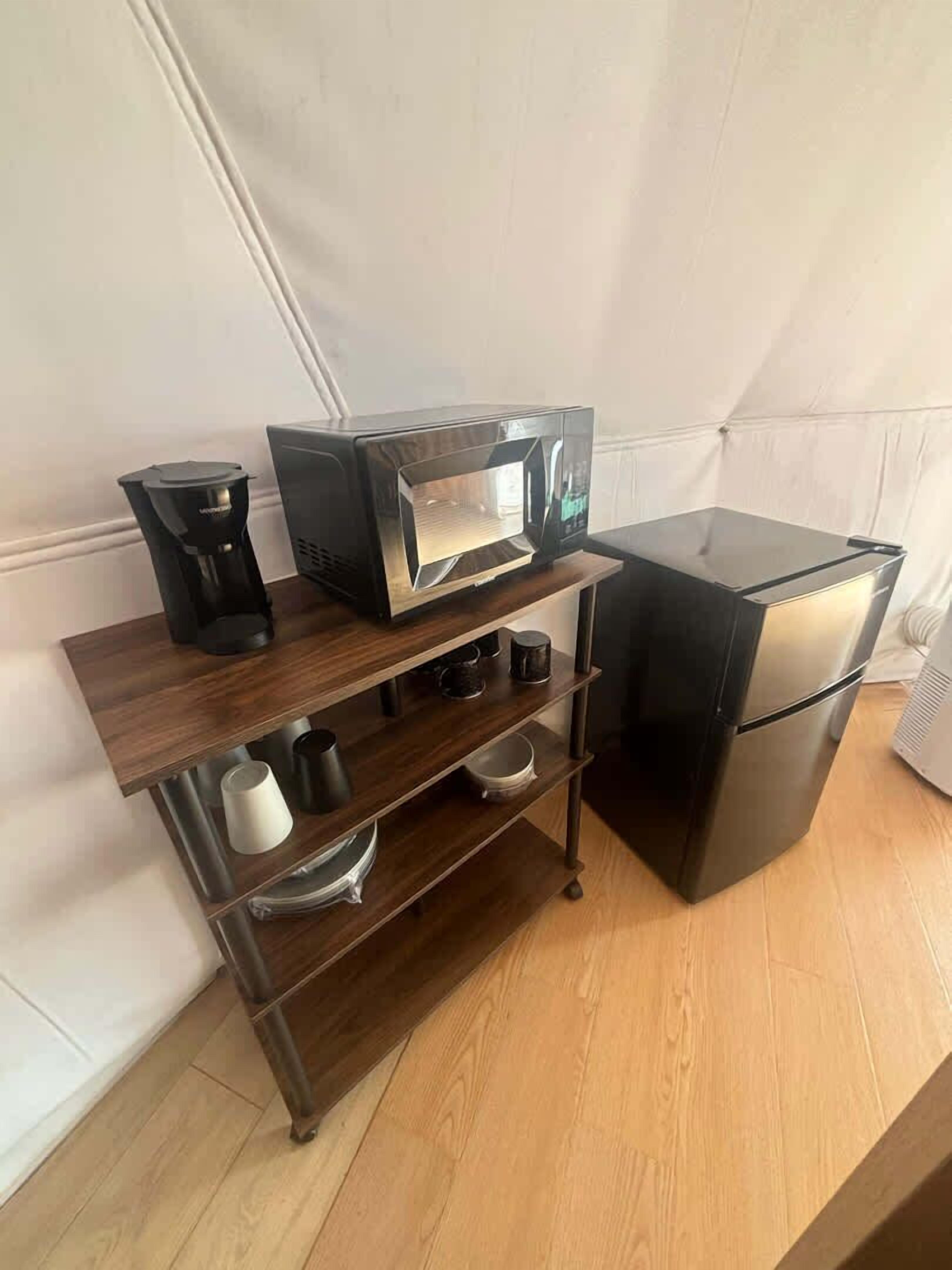 A kitchen with a microwave, coffee maker, and a refrigerator on a wooden shelf unit.