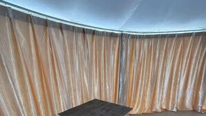 A tented room with a central table and benches, surrounded by beige curtains. - Lake view lovers nest (Denison)
