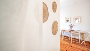 Une pièce minimaliste avec un mur blanc, un plancher en bois, une table ronde avec des chaises et trois œuvres d’art murales en fibres tressées.