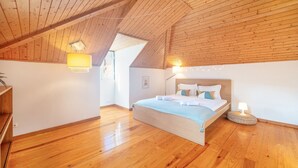 Une chambre avec un plafond en bois, un lit recouvert de draps blancs et une lampe de chevet.