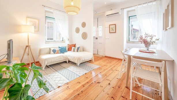 Un salon lumineux avec un plancher en bois, un ensemble de canapés blancs, une table à manger avec des chaises, une lampe sur pied et un luminaire suspendu.