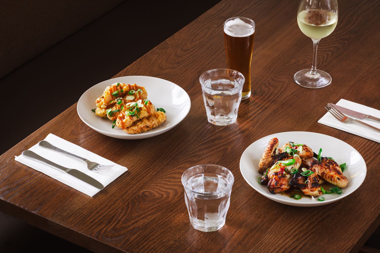 A wooden table with two plates of food, two glasses of water, and two glasses of beer.
