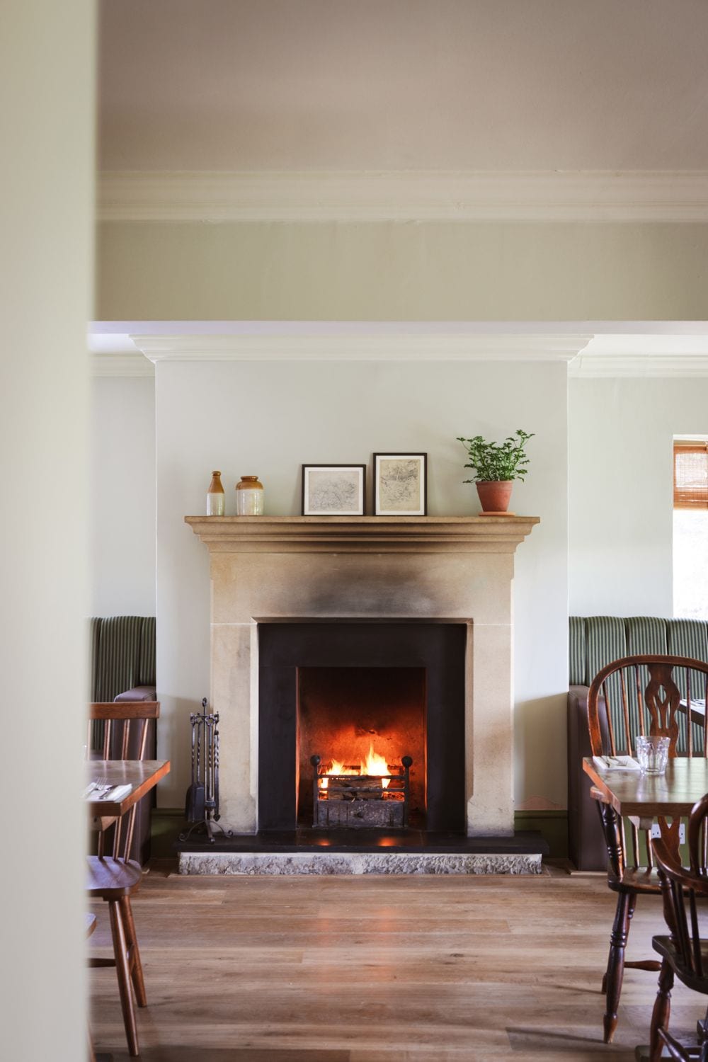 A fireplace with a fire, a mantel with decorative items, and a dining area with chairs and a table.