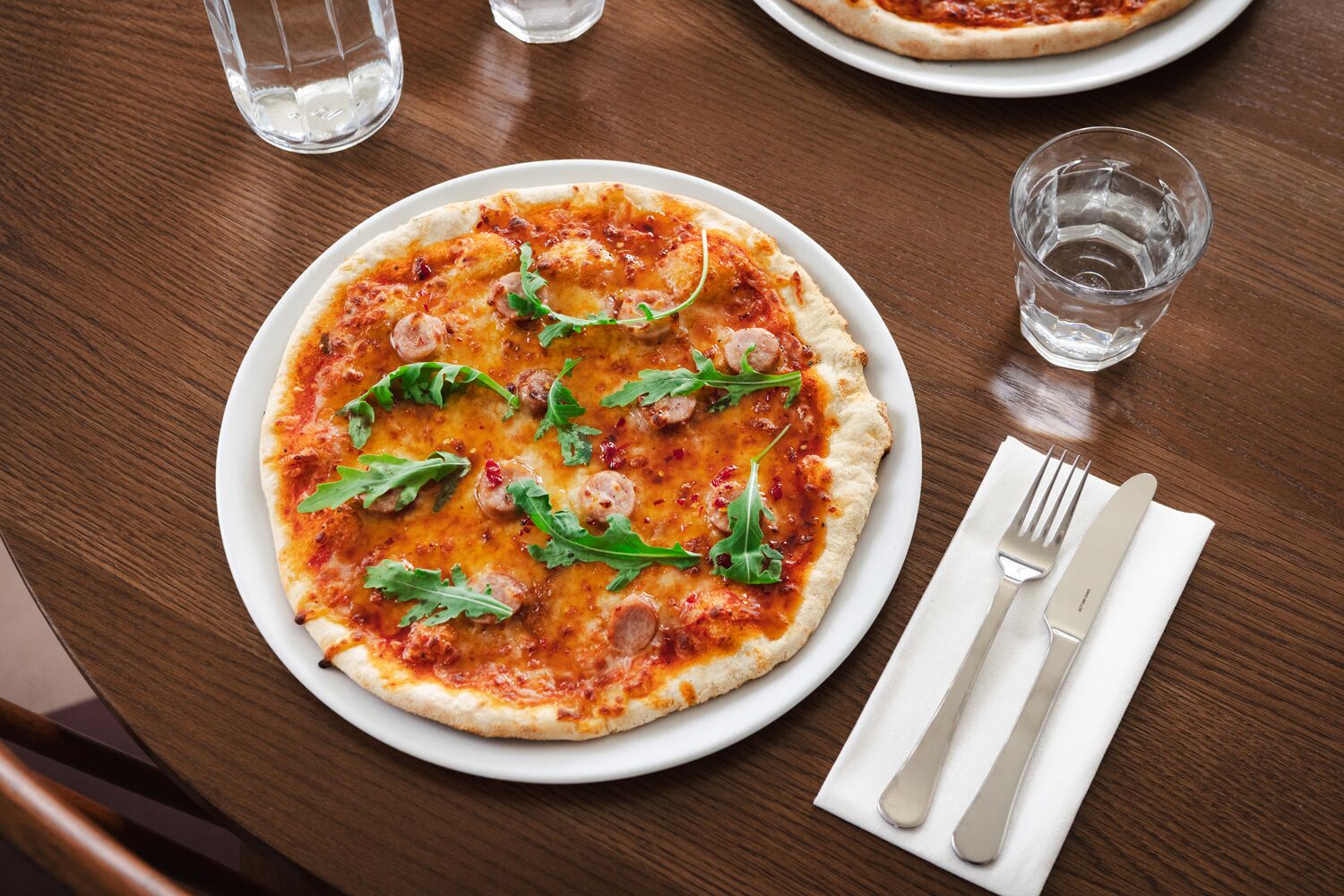 A pizza on a white plate with a fork and knife on a napkin beside it.