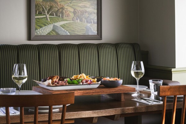 A dining table with a meal, two glasses of white wine, and a framed painting on the wall.
