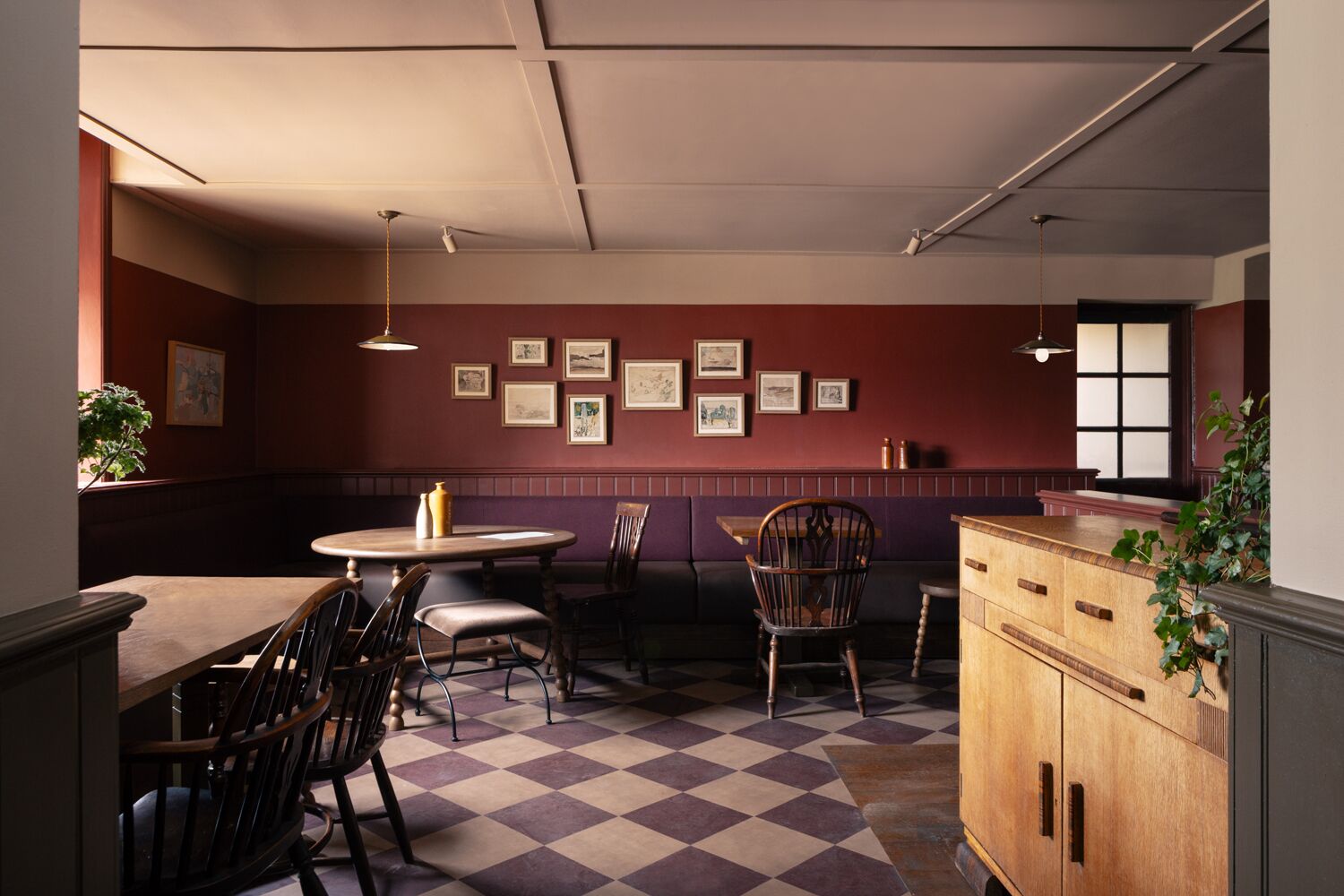 Un coin repas avec un sol à carreaux, des chaises en bois, une table ronde et des tableaux encadrés accrochés au mur.