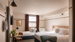 Ett hotellrum med två sängar, ett skrivbord med en stol, en krukväxt och ett fönster med gardiner.