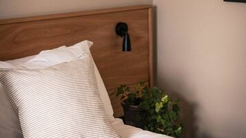 Un lit bien fait, agrémenté d’oreillers à rayures, d’une tête de lit en bois, d’une lampe de chevet et d’une estampe botanique encadrée accrochée au mur.