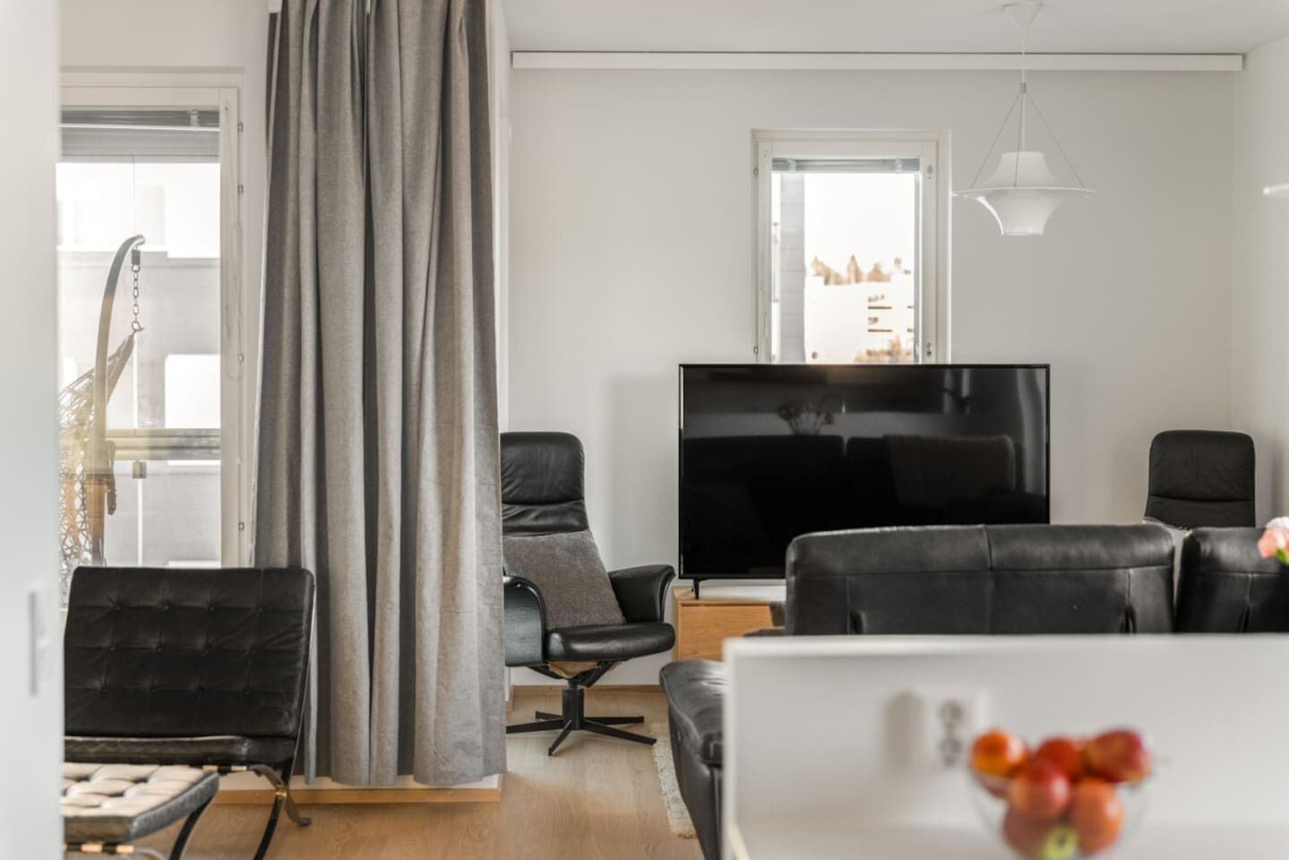 Ein modernes Wohnzimmer mit großem Flachbildfernseher, Ledersofas, einem Esstisch und Blick auf ein Gebäude durch ein Fenster.