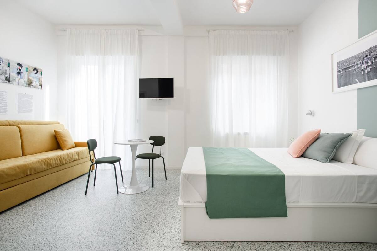 Una habitación de hotel moderna con sofá, cama, mesa y sillas, y televisión.