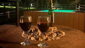 Una mesa con dos copas de vino y una botella, con montañas y una piscina iluminada al fondo.