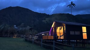 Una cabaña de madera con un amplio porche abierto, rodeada por una zona vallada y un paisaje montañoso.