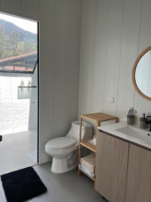 Ein modernes Badezimmer mit Toilette, Waschbecken und einem Holzwaschtisch. Über der Toilette befindet sich ein Dachfenster und es bietet sich ein Blick auf eine gebirgige Landschaft.