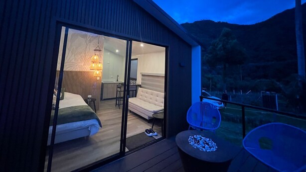 Una habitación de hotel moderna con un gran ventanal corredero que da a un balcón. La habitación tiene una cama, una mesita y una silla.